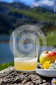 Green bottle and glass of natural Asturian cider made fromÂ fermented apples with view on Covadonga lake and tops of Picos de